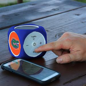 A hand adjusts a blue Florida Gators MX-300 Cubio Bluetooth® Speaker beside a smartphone on a wooden table.
