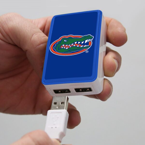 A hand holding a blue QuikVolt Florida Gators WP-200X Classic Dual-Port USB Wall Charger, featuring a usb cable connected to it.
