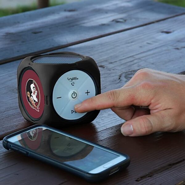 A person's finger pressing the play button on a FSU Seminoles MX-300 Cubio Bluetooth® Speaker next to a smartphone on a wooden table.