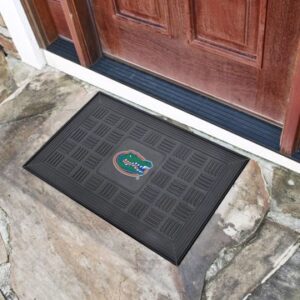 A Florida Gators Vinyl Door Mat featuring the florida gators logo, placed at the entrance of a house with a brown door and stone flooring.