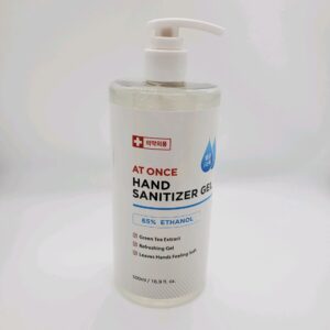 A bottle of At One 16oz Hand Sanitizer with a pump dispenser, containing 65% ethanol and green tea extract, on a white background.