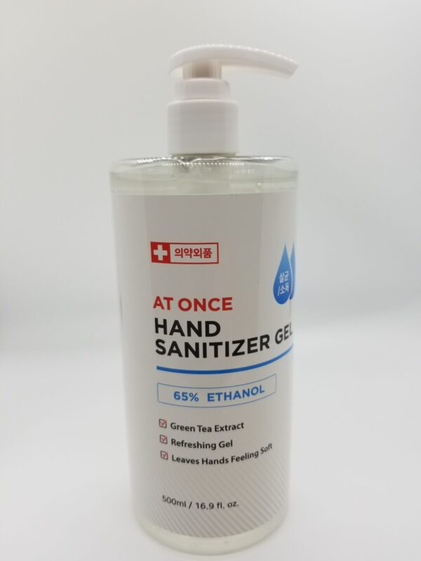 A bottle of "At One 16oz Hand Sanitizer" with 65% ethanol, green tea extract, and claims to leave hands soft, on a white background.