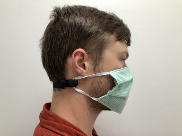 Profile view of a young man wearing a green surgical mask secured with an ELASTIC MASK CLIP EXTENDER 5/Pack around his head.