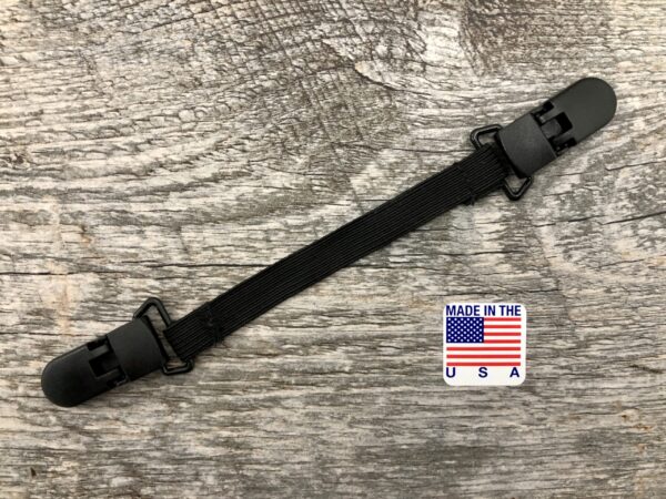 Adjustable black strap with plastic buckles on a wooden surface, featuring a "made in the usa" label with an american flag for the ELASTIC MASK CLIP EXTENDER 5/Pack.