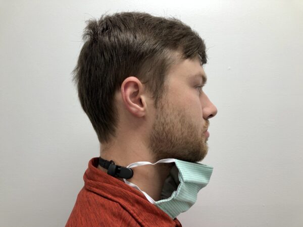 Profile view of a young man with a beard, wearing a red shirt and an ELASTIC MASK CLIP EXTENDER 5/Pack hanging off one ear, against a plain white background.