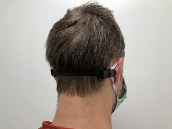 Rear view of a person wearing a ELASTIC MASK CLIP EXTENDER 5/Pack with a black strap adjuster around their head, focusing on the hair and ear.