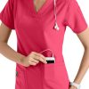 A smiling female healthcare professional in a CROSS FLEX V-NECK MEDIA SCRUB TOP C12110 placing a smartphone into her pocket, with a stethoscope around her neck.