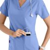 A smiling healthcare professional in CROSS FLEX V-NECK MEDIA SCRUB TOP C12110 placing a mobile device into her pocket.