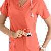 Smiling female healthcare worker in Coral Cross Flex V-Neck Media Scrub Top C12110 using a smartphone, with a stethoscope around her neck, isolated on a white background.