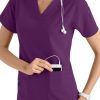 A smiling healthcare worker in a CROSS FLEX V-NECK MEDIA SCRUB TOP C12110, placing a device with headphones into her pocket.