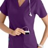 Smiling female healthcare worker in CROSS FLEX V-NECK MEDIA SCRUB TOP C12110 placing a smartphone in her pocket, wearing a stethoscope around her neck.