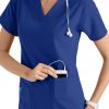 A smiling healthcare worker in a CROSS FLEX V-NECK MEDIA SCRUB TOP C12110 with a stethoscope around her neck, inserting a smartphone into her pocket.