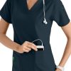 A smiling female nurse in a CROSS FLEX V-NECK MEDIA SCRUB TOP C12110, placing a device into her pocket, with a stethoscope around her neck.