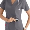 A smiling healthcare professional in a CROSS FLEX V-NECK MEDIA SCRUB TOP C12110 puts a mobile device into her pocket, with a stethoscope around her neck.