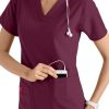 A smiling healthcare worker in a CROSS FLEX V-NECK MEDIA SCRUB TOP C12110 with a stethoscope around her neck, placing a device in her pocket.