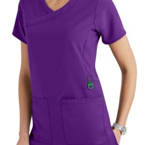Woman in purple medical scrubs with a v-neck, short sleeves, and multiple pockets, standing with one hand lightly resting on her hip.
