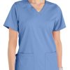 A woman in a Comfort Utility V-Neck Top (Liberty C13106) with short sleeves and v-neck, featuring front pockets.