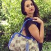 A woman with dark hair posing in a lush garden, holding The Patriot Handbag (Florida Gators) over her shoulder.