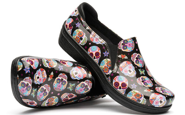 A pair of Moxy by Klogs Footwear slip-on shoes with a colorful sugar skull pattern on a black background.