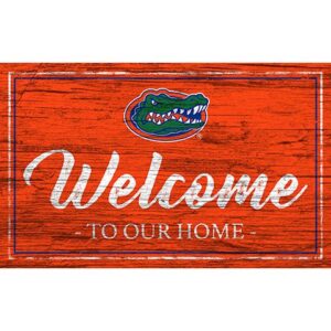 A University of Florida Team Color Welcome 11x19 Sign with the text "welcome to our home" painted in white, featuring a florida gators logo in the top left corner on a red background.