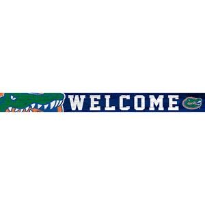 A University of Florida 16in. Welcome Strip featuring a blue background, white text, and a green alligator on either side, one wearing a hat with the university of florida logo.