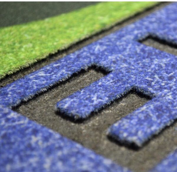 Close-up of a textured, Miami Hurricanes Crumb Rubber Door Mat with an embossed letter "e" in a contrasting deep shade, surrounded by green and black sections.