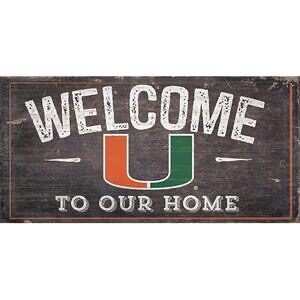 A rustic wooden sign with the word "welcome" in large white letters, a green and orange "u" below it, and the words "to our home" in smaller white letters.