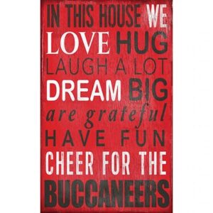 Decorative red and white sign with phrases like "in this house we love, hug, laugh a lot, dream big" and "cheer for the buccaneers" in various fonts.