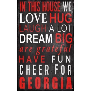 Decorative sign with phrases "in this house we love, hug, laugh a lot, dream big, are grateful, have fun, cheer for georgia" in white/red letters on a black background.