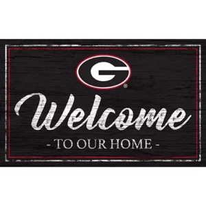 A decorative welcome sign featuring a prominent letter "g" logo, styled with a distressed black wood background and the words "welcome to our home" in white cursive and block letters.