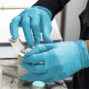 Hands in AMMEX Blue Nitrile Exam Latex Free Disposable Gloves handling medication, with focus on opening a pill bottle over a prescription bag.