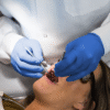 A dentist in white coat and AMMEX Professional Cerulean Nitrile PF Exam Gloves performing a dental procedure on a female patient.