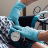 A healthcare professional in AMMEX Blue Nitrile Exam Latex Free Disposable Gloves measures a patient's blood pressure using a sphygmomanometer.